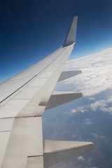 Fototapeta premium Wing of an airplane flying above the clouds. people look at the sky from the window of the plane, using air transport to travel. back light sun beam