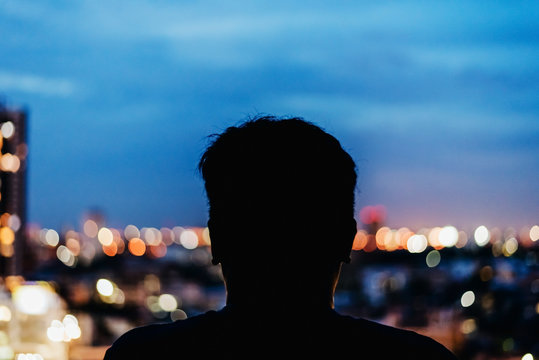Man watching the view from skyscraper. Contours of the man to background night city. Black man silhouette in the window of a skyscraper. Dark outline man watching night city.