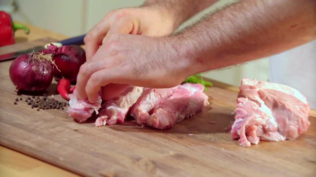Cutting meat on a wooden kitchen board. The man cuts meat. The man undresses meat for frying. The man cuts pork