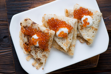 Above view of crepes served with sour cream and salmon caviar