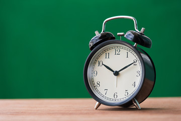 black alarm clock on wooden table with green background