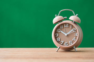 alarm clock on wooden table with green background