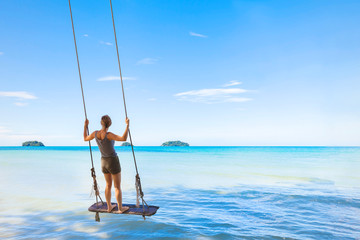 Happy girl swinging on rope swing, paradise sea in background