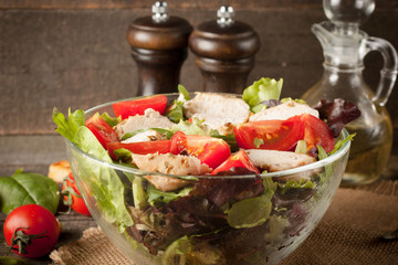 Fresh salad made of tomato, ruccola, chicken breast, arugula, crackers and spices. Caesar salad in a white, transparent bowl on wooden background