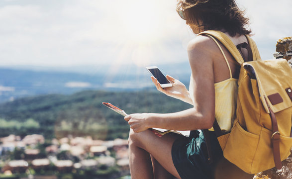 Hipster young girl with bright backpack looking at phone and map. Said view tourist traveler on background mountain, blue sea, sun flare. Mockup for text message. Female hands using smartphone
