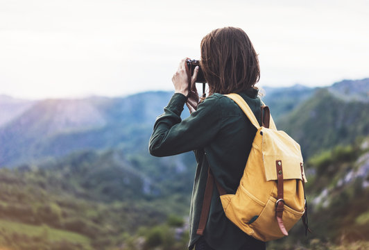 Tourist traveler photographer taking pictures of landscape on vintage photo camera on background valley view mockup sun flare, hipster girl with backpack enjoying sunset on peak of foggy mountain