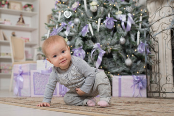 The baby girl is sitting next to the Christmas tree and boxes with gifts