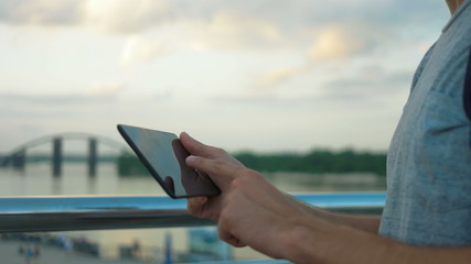 Smiling man using his tablet in front of the river.