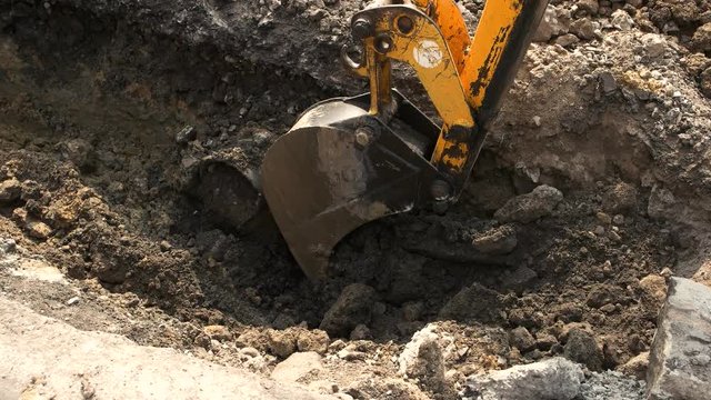 Bucket of excavator in motion. Machine digs a pit. Metal and dirt. Building a trench for cables.