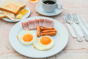 Breakfast with Fried egg, Ham, Sausage and black coffee on marble table.