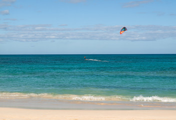 Unknown kitesurfer surfing on a flat azure water of Atlantic ocean in Corralejo, Fuerteventura, Canary islands, Spain
