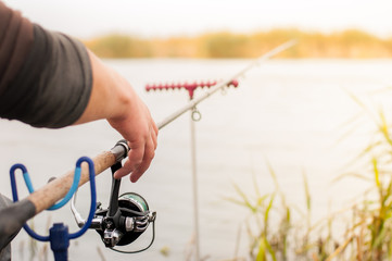 Hand with rod and reel on the lake.