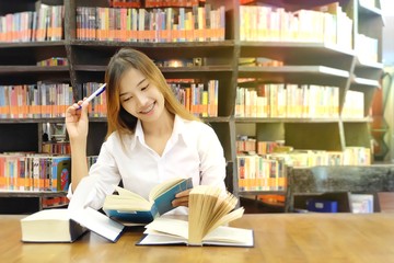 Portrait of a young student reading a book in a library.