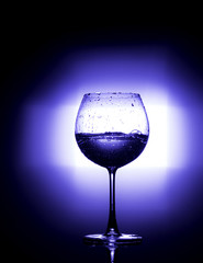 Pouring water into wine glass with black background blue white balnce