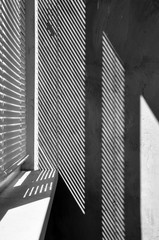 Geometric black and white composition. The plane of the plaster wall with a structural graphic shadow falling from the blinds. Vertical view.