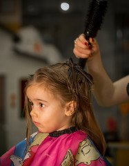 Beautiful little girl with long hair, cuts hair in the barbershop, hairdressers