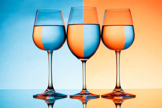 Three wineglasses with water over blue and orange background.