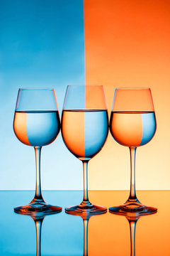 Three wineglasses with water over blue and orange background.