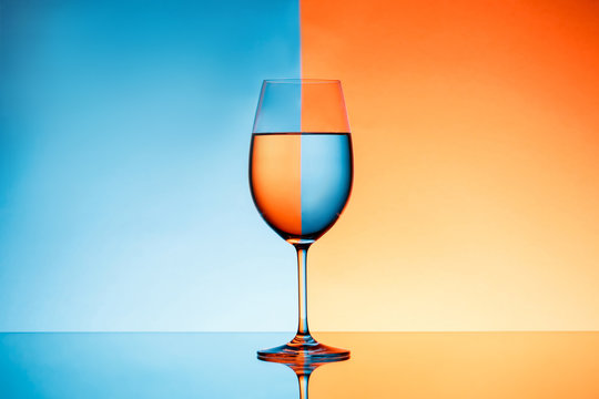 Wineglass with water over blue and orange background.