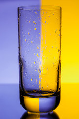 Empty glass with water drops over purple and yellow background.