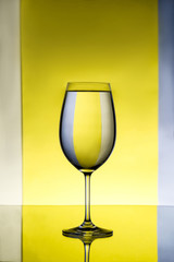 Wineglass with water over grey and yellow background.