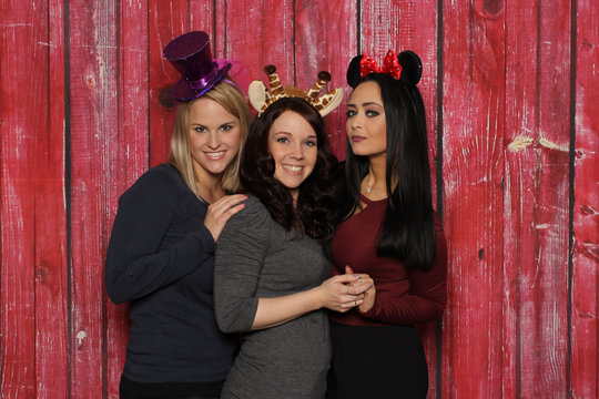 3 süße Mädchen vor einer Fotobox - 3 Mädchen mit Kopfbedeckungen vor einem roten Hintergrund