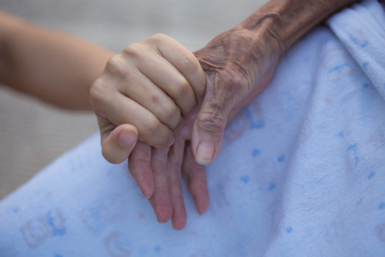 Old and young holding hands on light background, closeup