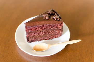 Piece of dark chocolate cake on white dish with wooden spoon ready to eating