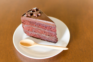 Piece of dark chocolate cake on white dish with wooden spoon ready to eating