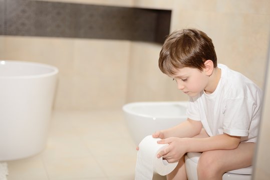 Little 7 years old boy sitting on toilet.