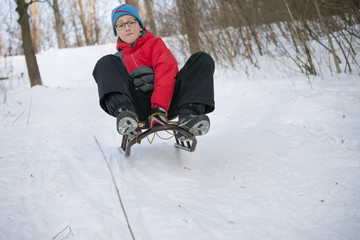 Fototapeta na wymiar Teenage boy in glasses quickly moves down on a sled with snow slides,.motion blur