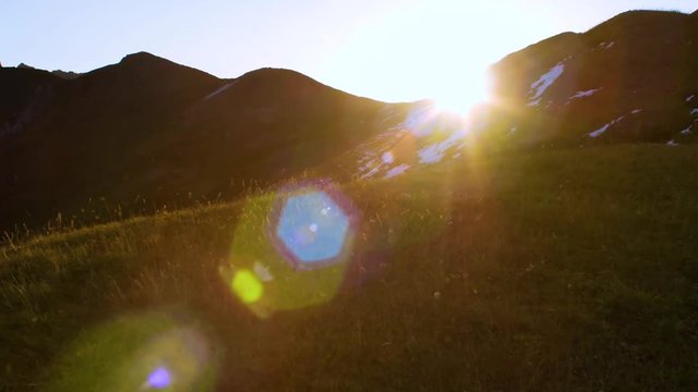 Sun rising from behind snow mountains. Tight shot with a beautiful lens flare moves through frame