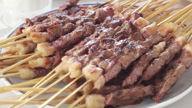 Hot roasted meat shish kebab with skewer on plate. Customers taking kebabs with hands at restaurant