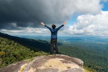 Young successful man open arms on mountain peak above the forest