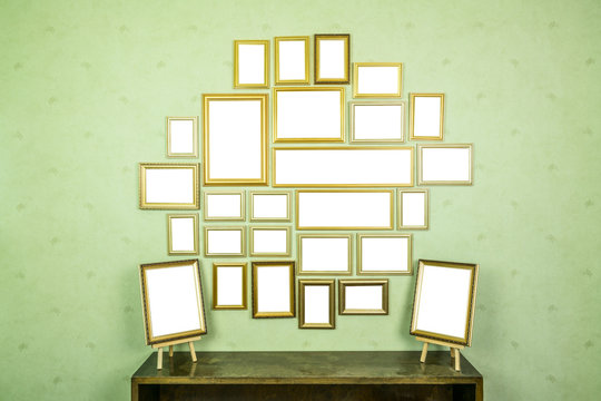 Many empty golden wooden frames with copy space on green wallpapered wall and bookshelf.