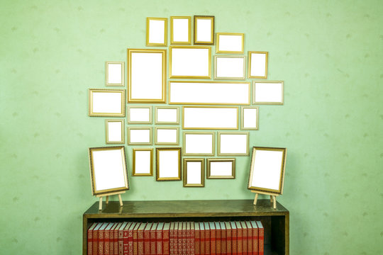 Many empty golden wooden frames with copy space on green wallpapered wall. Bookshelf with red books.
