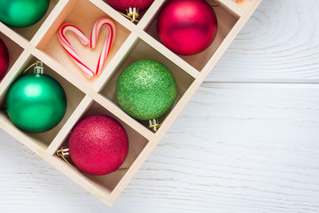 Preparation for Christmas: festive balls and candy cane in wooden box on white wooden table, horizontal, copy space