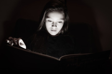 Young teen girl reading a book in the dark