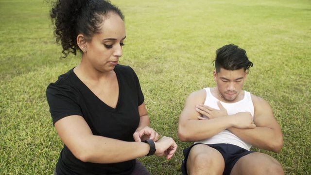 Handheld scene of a young man timing his workout buddy while she does her sit-ups.