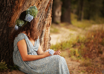 Kobieta w wianku na głowie siedząca pod drzewem - obrazy, fototapety, plakaty