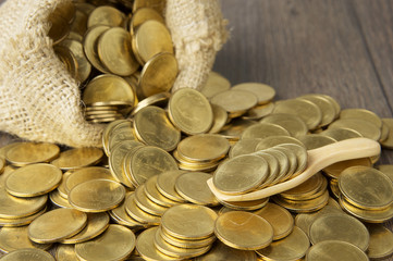 Close up gold coins in wooden spoon with brown sack