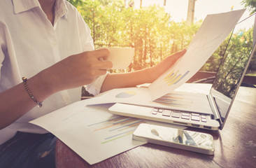 Business woman analyzing graph document with laptop and holding coffee vintage tone.