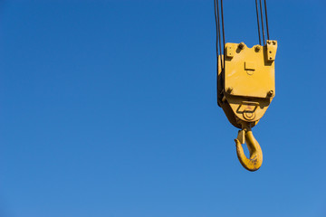 Fototapeta premium A yellow crane hook suspended against a blue sky
