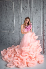 Beautiful young girl with long wavy hair holding a bouquet of flowers in pink dress-the cloud is in interior