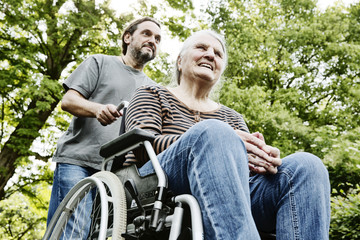Fototapeta na wymiar Sohn schiebt seine demenzkranke Mutter, Seniorin, im Rollstuhl