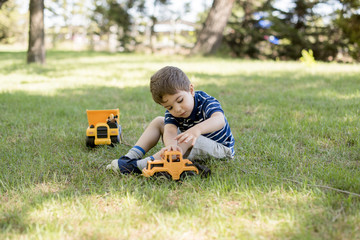 Fototapeta premium Kid, 4 years, playing with toys cars and trucks at field