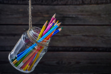 Colored pencils in a glass jar. On rustic background.