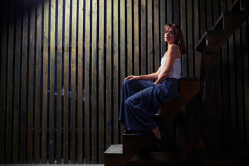 Pleased female model is sitting on the edge of the wooden step,