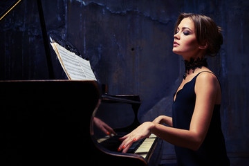 Young elegant woman in evening dress playing piano in studio