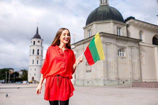 Young female tourist standing with lithuanian flag on the cathedral square in front of the famous basilica in Vilnius. Having great vacations in Lithuania